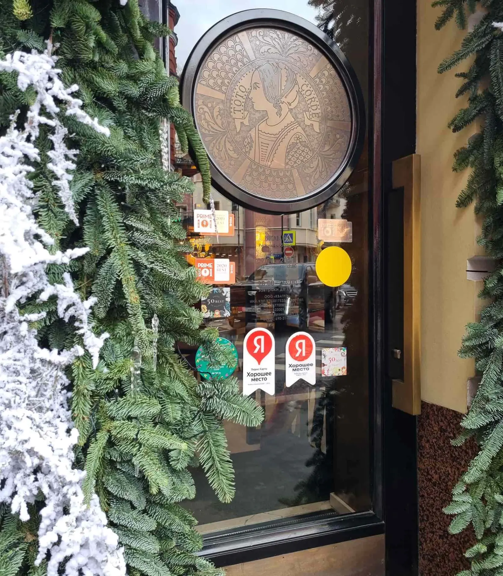 На двери кофейни наклеены отметки о наградах и рейтингах: выбор пользователей «Яндекс Карт», PRIME, которые указывают на популярность места